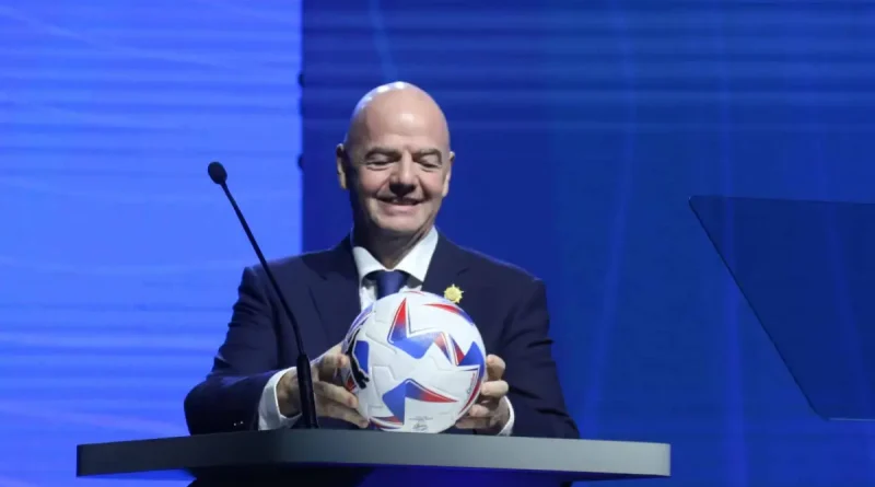 Gianni infantino sosteniendo un balon en un podio y vistiendo un traje negro con camisa blanca.